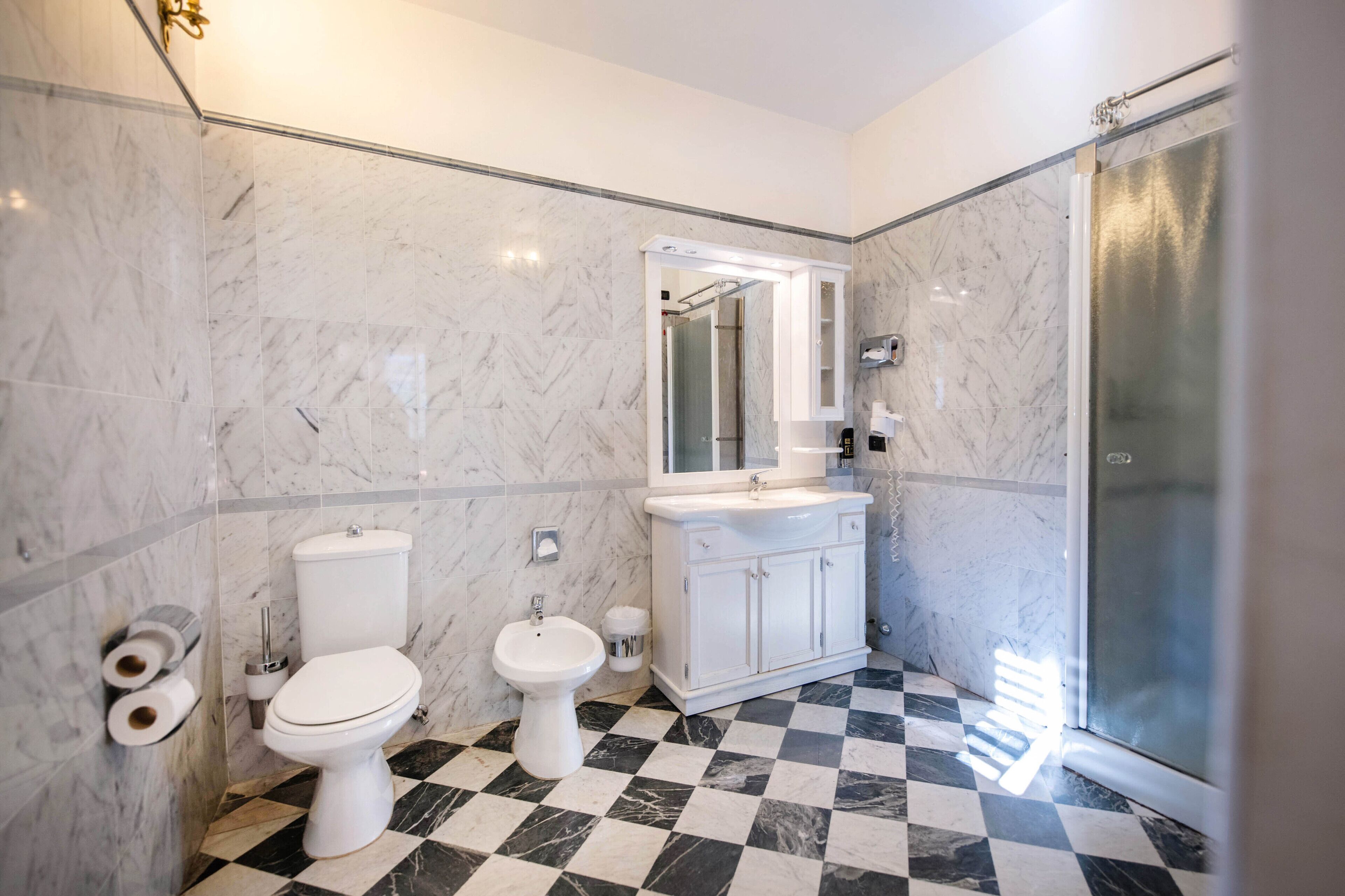 A bathroom with a marble floor, a toilet, a bidet, a sink with a mirror, and a shower area.