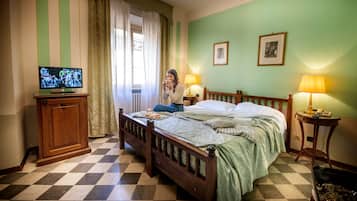 Ein Hotelzimmer mit Schachbrettmuster-Boden, einem Holzbett, einem Fernseher auf einem Schrank und zwei Nachttischlampen.