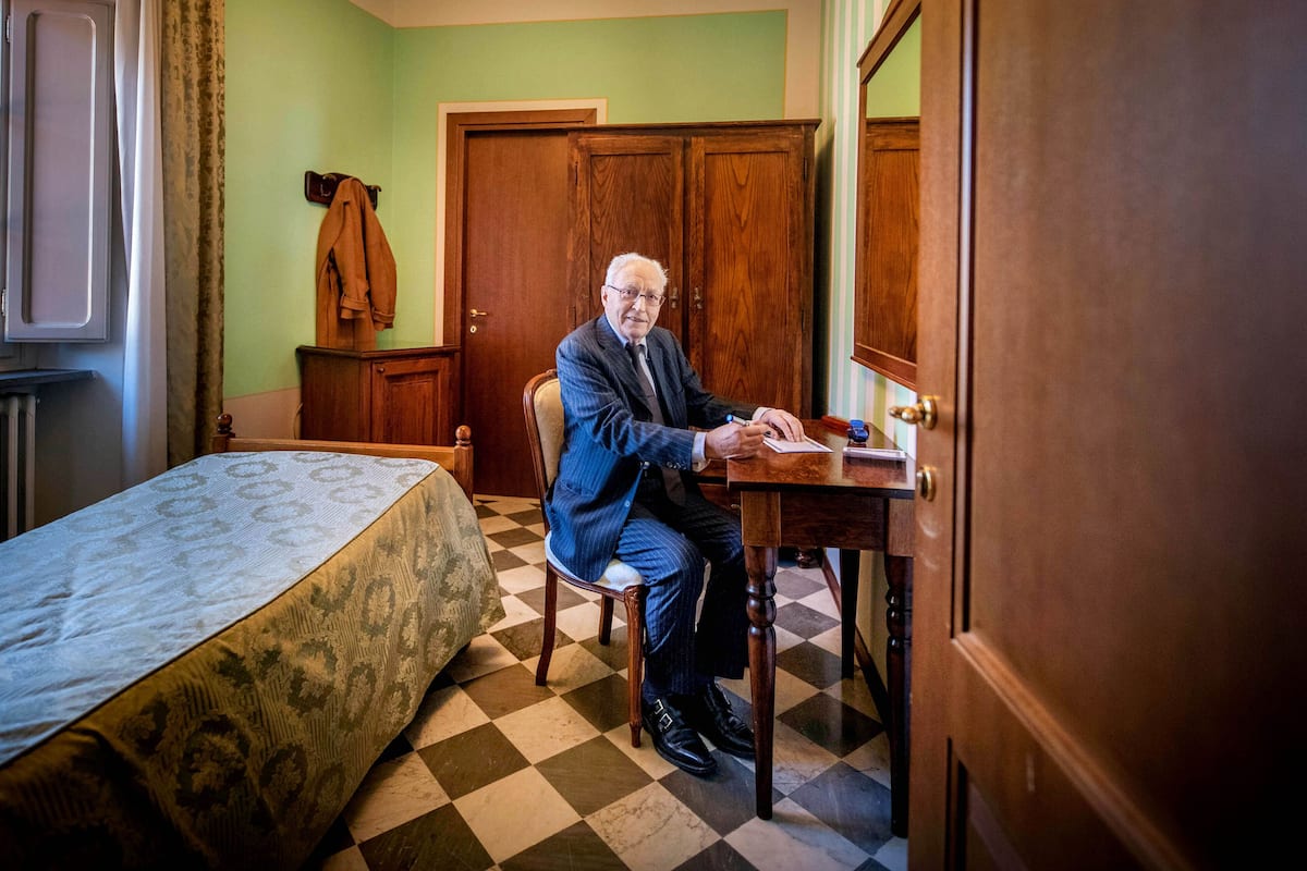 A room with a bed, a wooden wardrobe, and a chair.