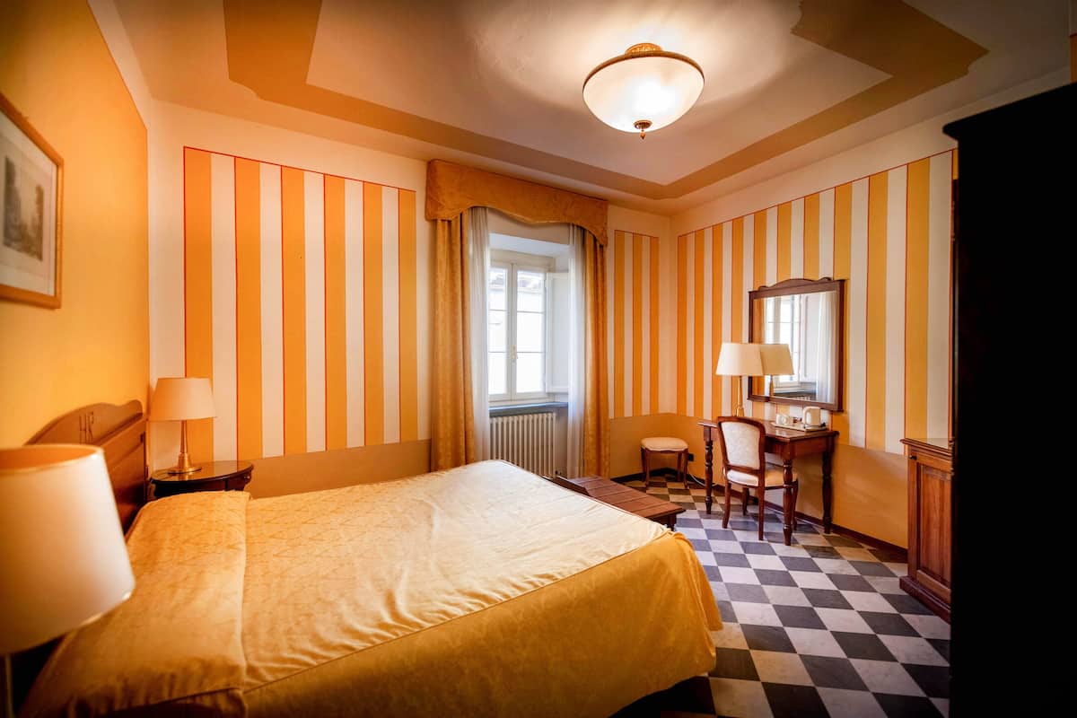 A hotel room with a bed, a desk, a chair, a lamp, and a window with curtains.
