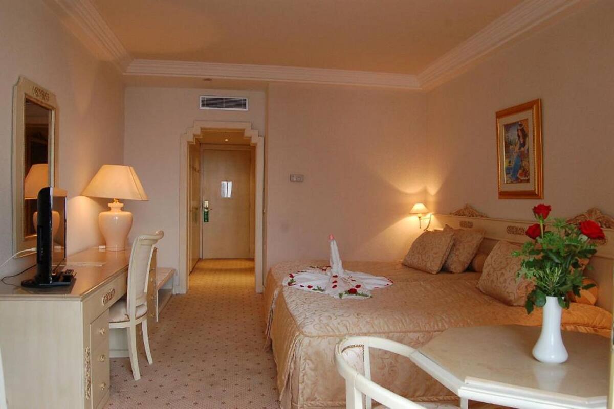 Habitació d'hotel amb un llit, escriptori amb làmpada, cadira, taulell de nit amb un ram de flors i un quadre a la paret.