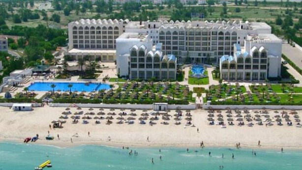 Un grand hôtel doté d’une cour intérieure, d’une piscine et d’un espace plage aménagé avec des parasols.