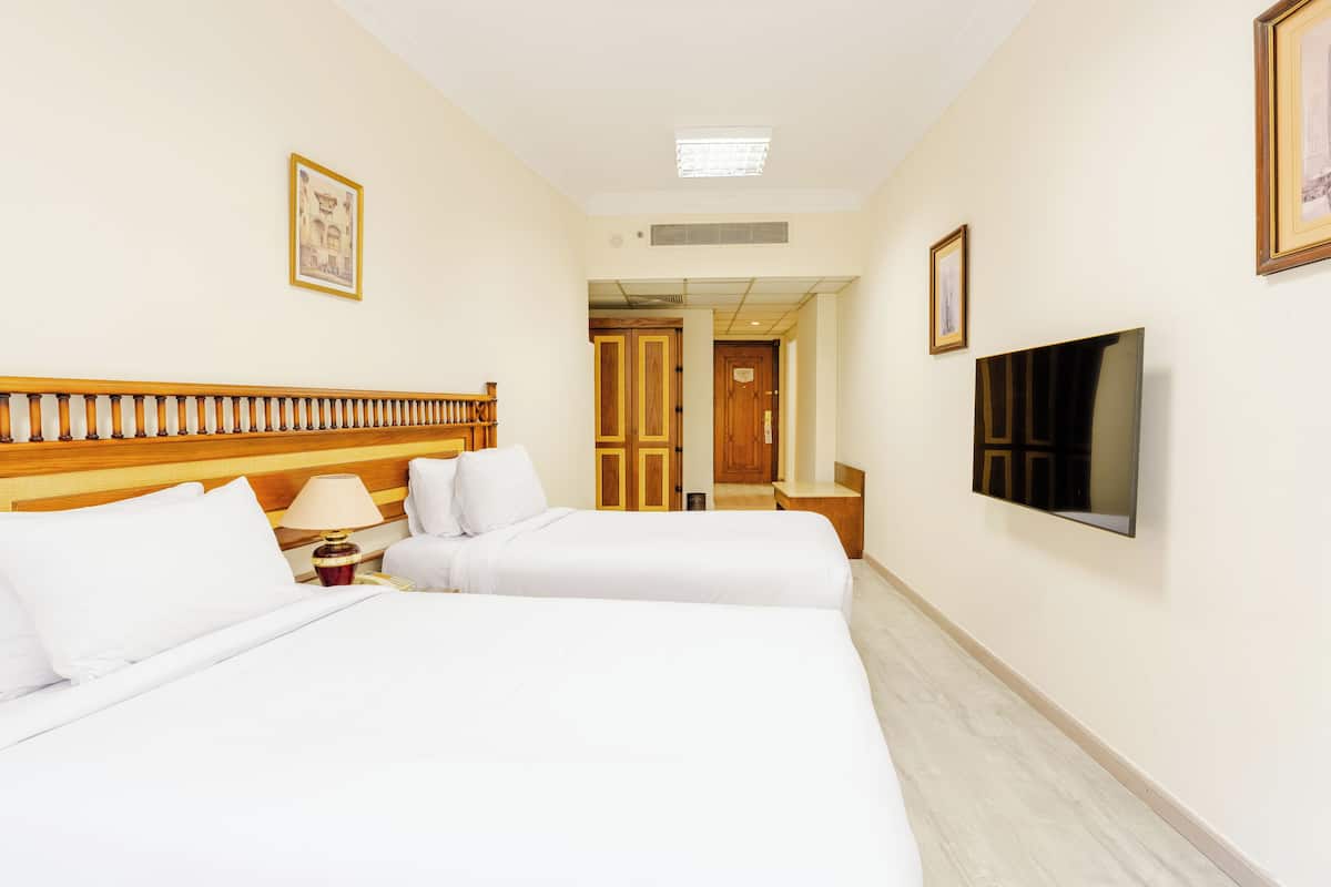 A hotel room with two beds, a TV, and a wooden headboard.