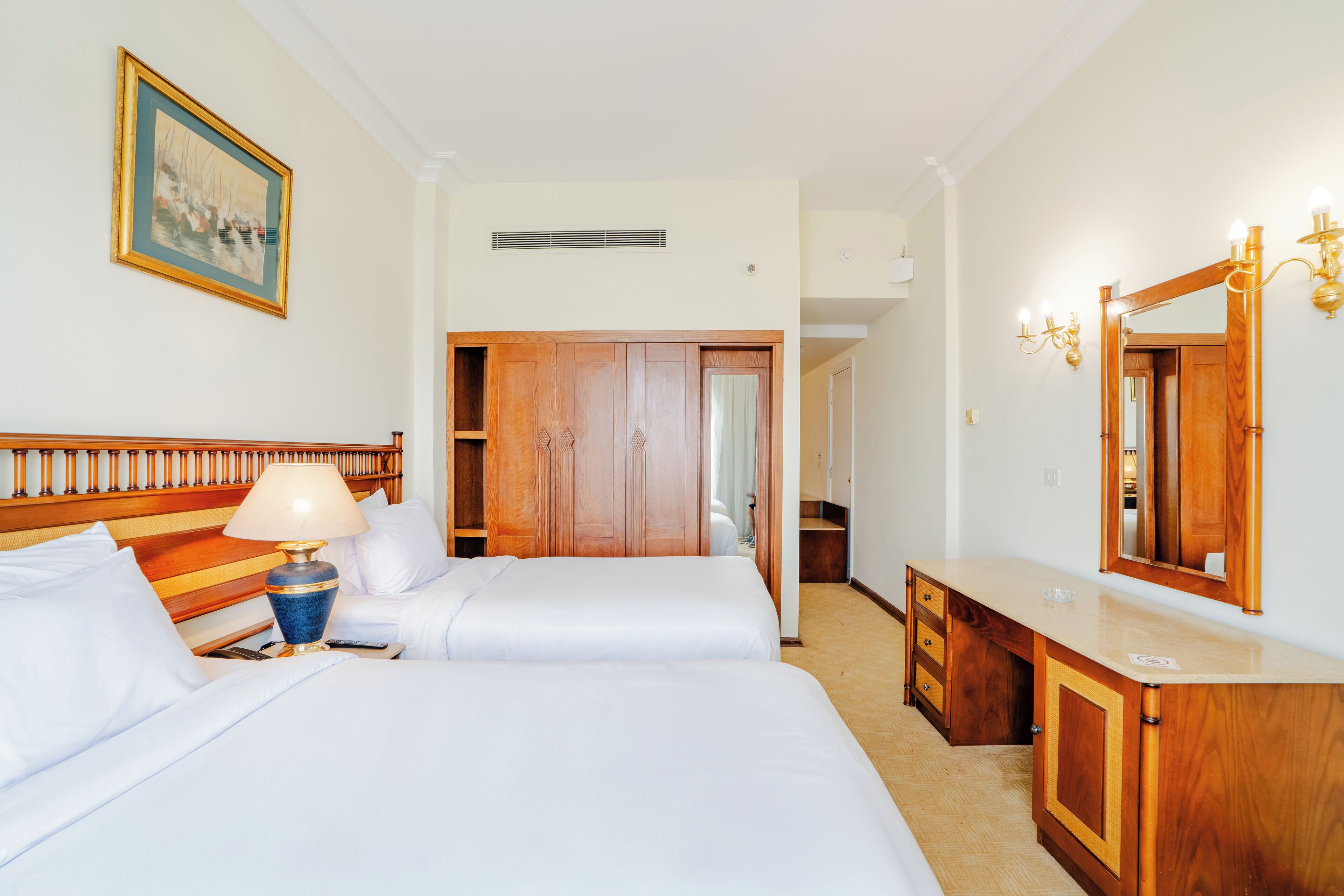 A hotel room with two beds, a wooden wardrobe, a dressing table, and a mirror.