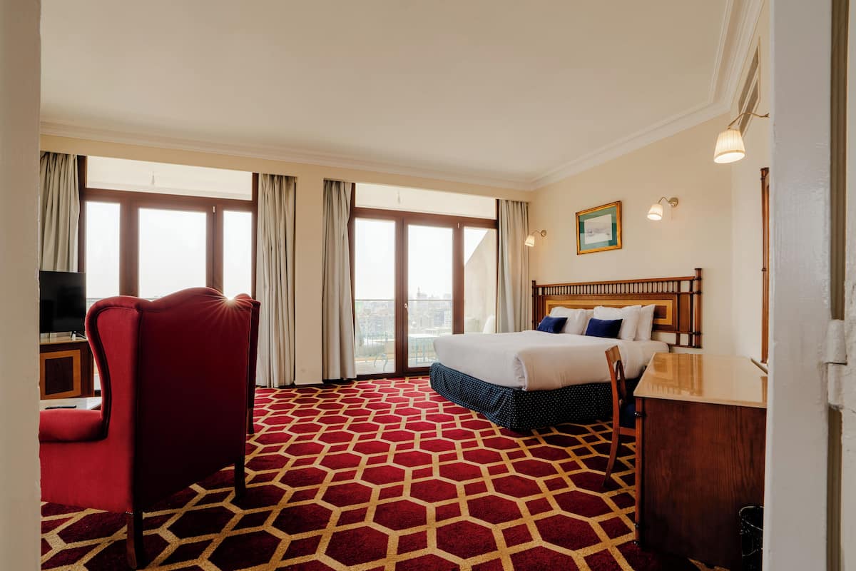 A hotel room with a large bed, a desk, a red chair, and a television.