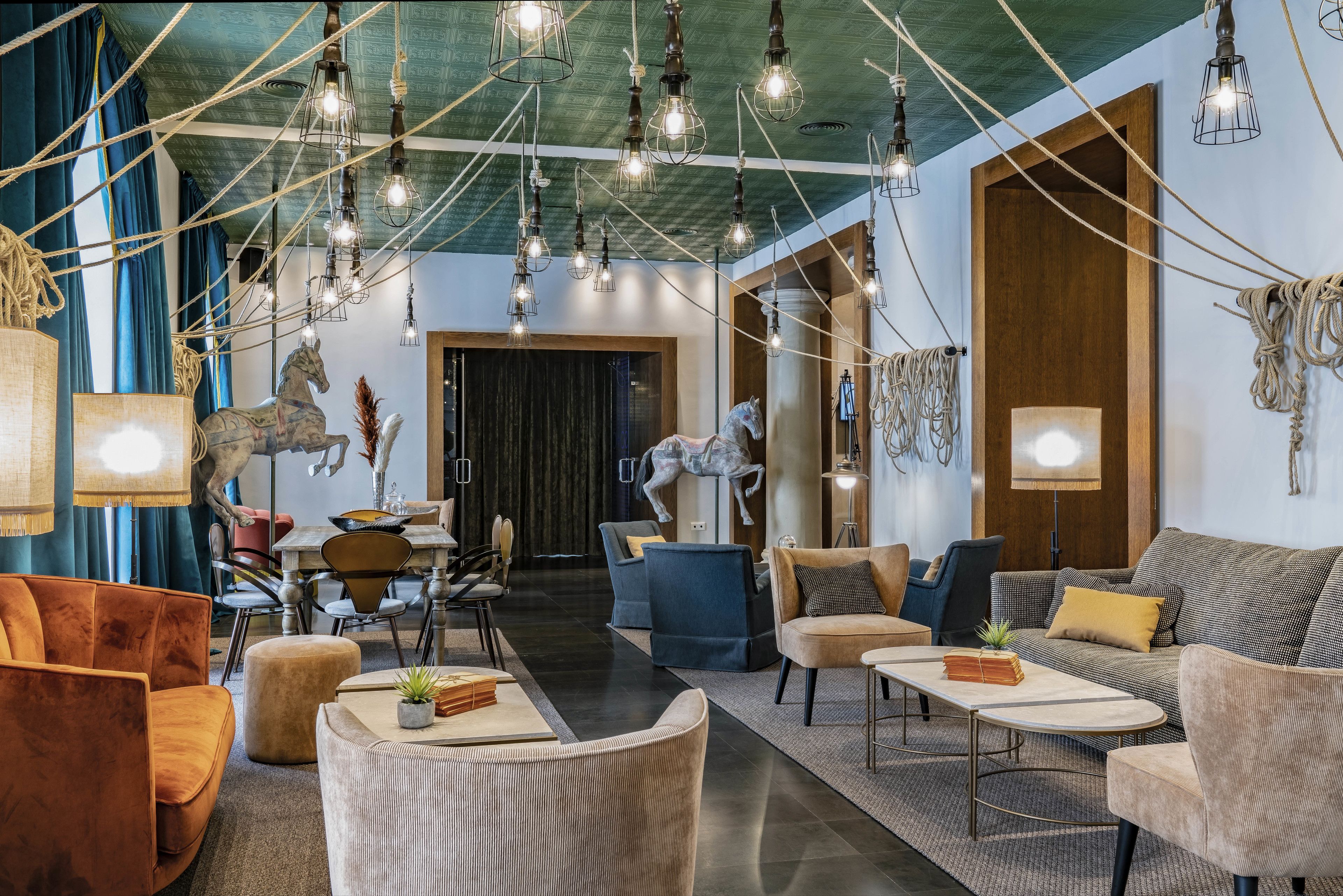 A spacious lobby with a modern design, featuring a mix of seating areas, a dining setup, and decorative elements like sculptures and hanging lights.