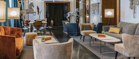 A spacious lobby with a modern design, featuring a mix of seating areas, a dining setup, and decorative elements like sculptures and hanging lights.