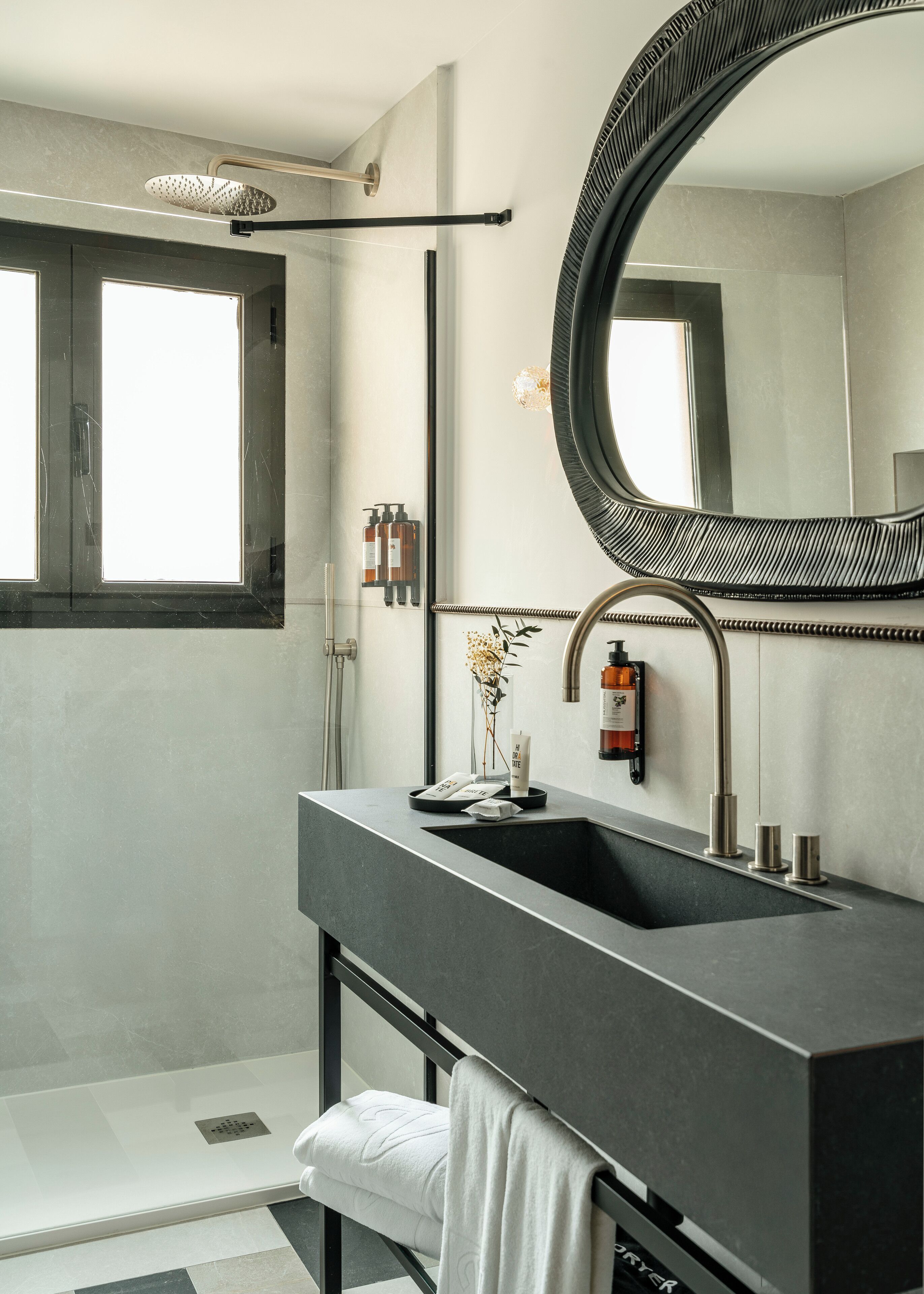 A modern bathroom with a large mirror, a showerhead, a sink, and toiletries.