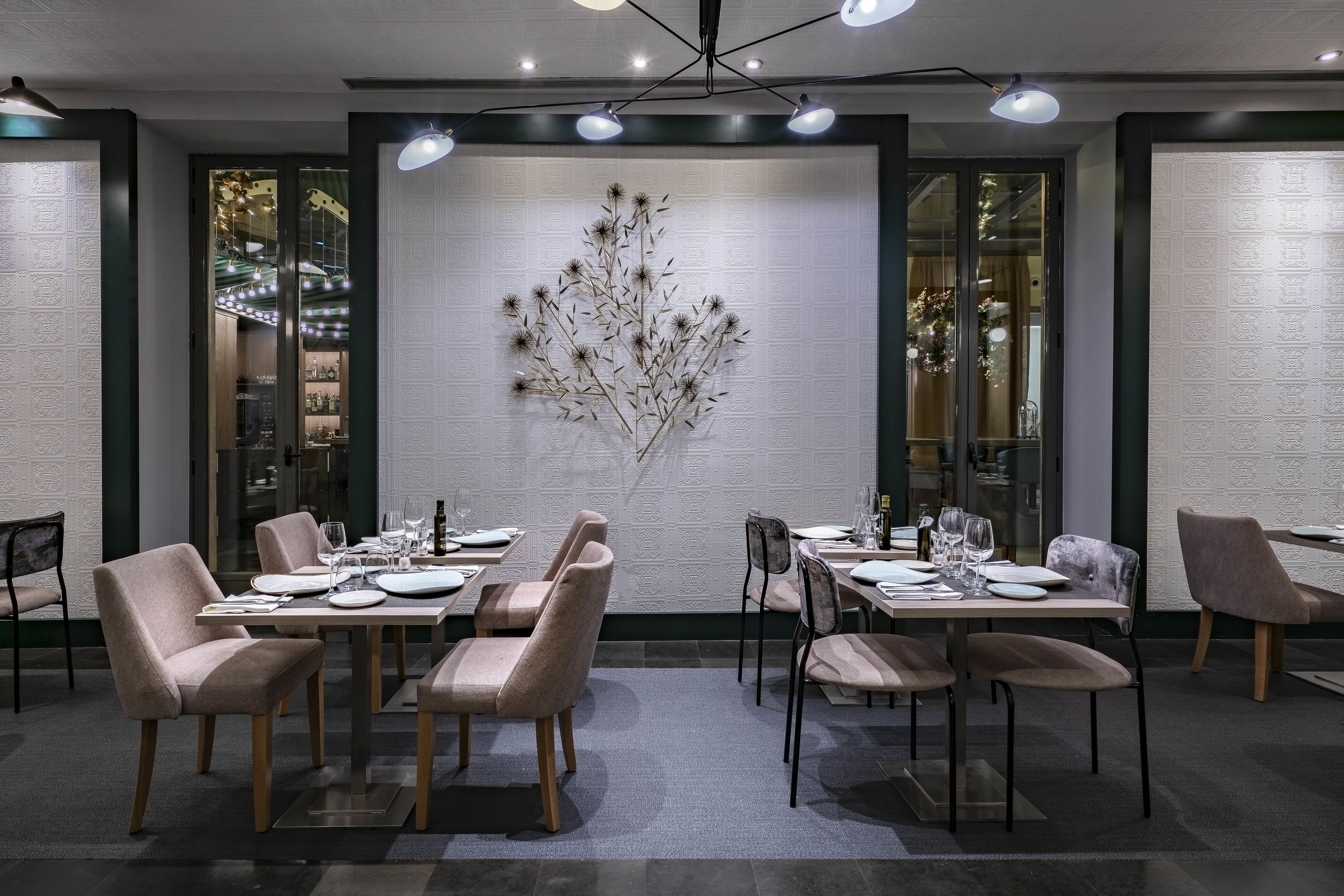 Una sala da pranzo moderna con tavoli apparecchiati per quattro persone, caratterizzata da sedie dai colori chiari e un elemento decorativo a parete.