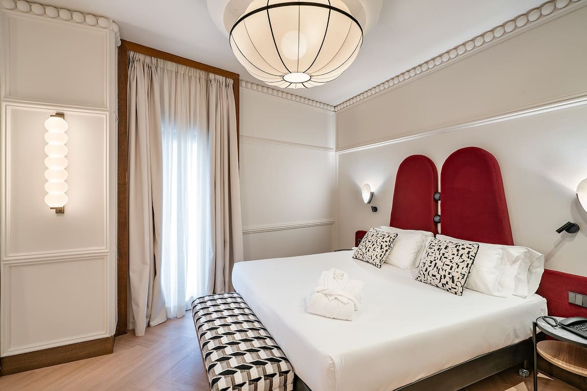 Une chambre d’hôtel avec un grand lit, une banquette, un bureau et un lustre.
