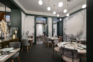 A modern restaurant interior with round tables, grey chairs, and a dark floor.