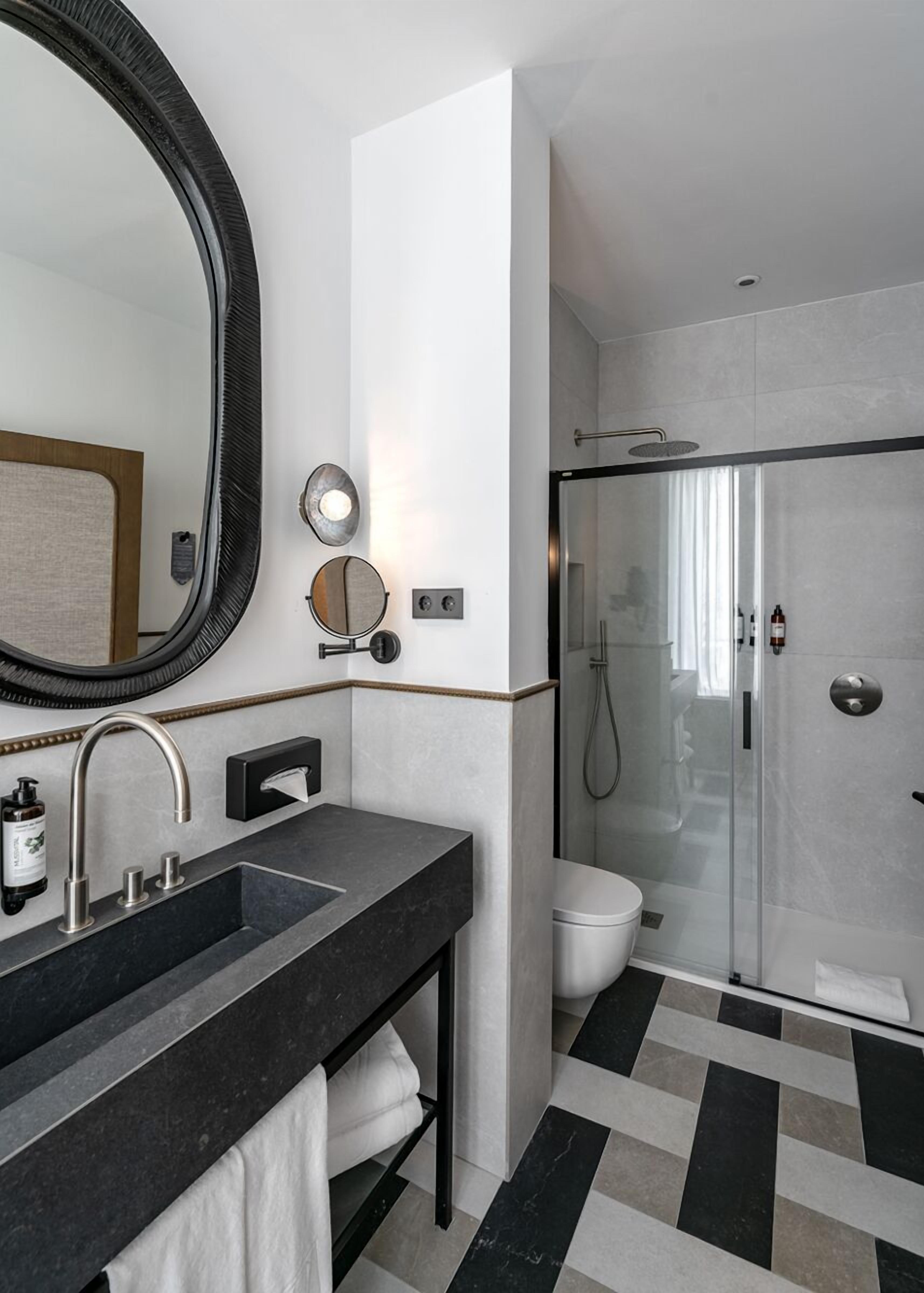 A modern bathroom with a large mirror, a sink with a towel rack, a toilet, and a shower area.
