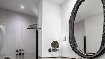 A modern bathroom with a glass-enclosed shower, a large oval mirror, and a black sink with a towel rack.