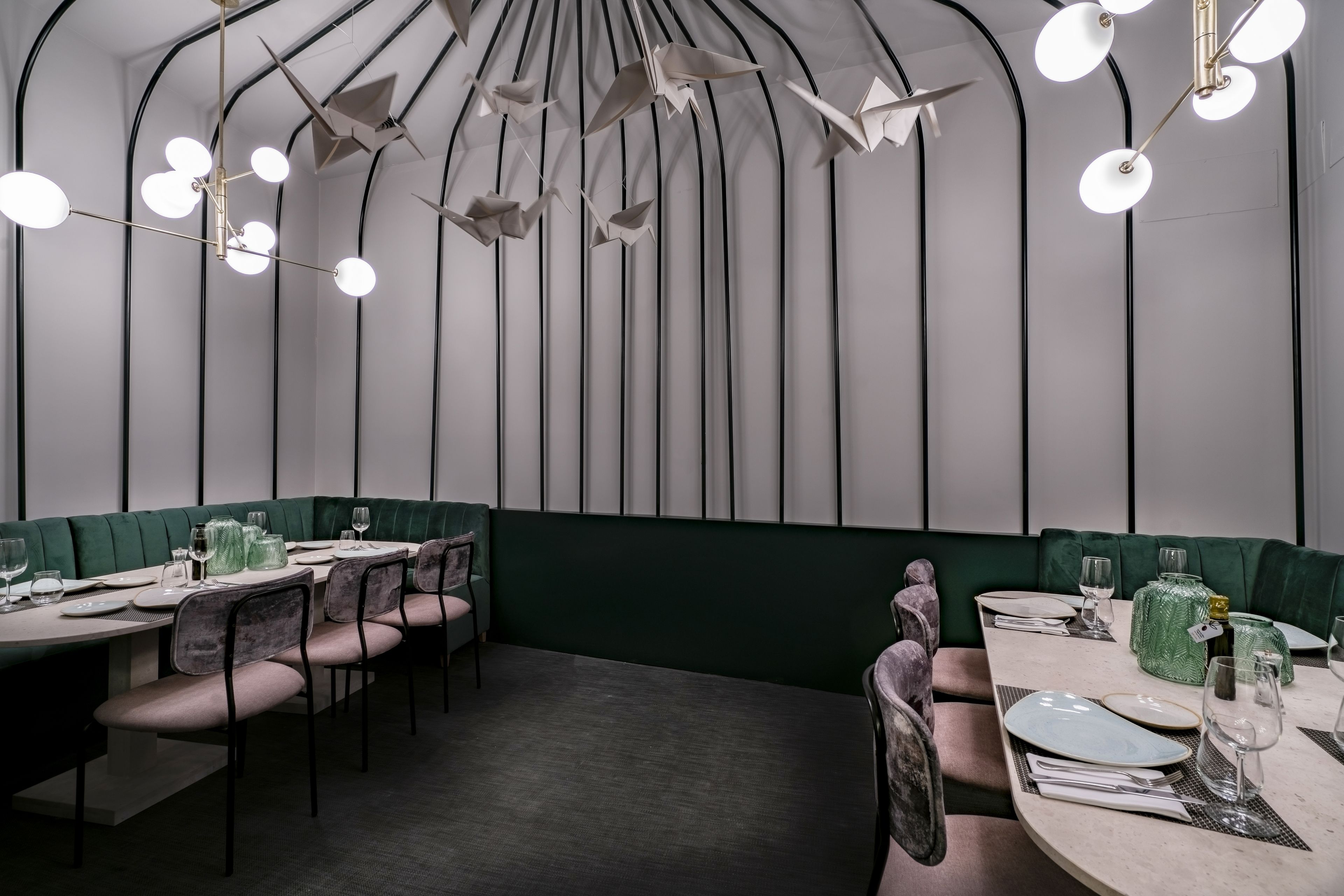 Een moderne eetruimte met een lange tafel, groene bekleden zitbanken en een unieke lamp.