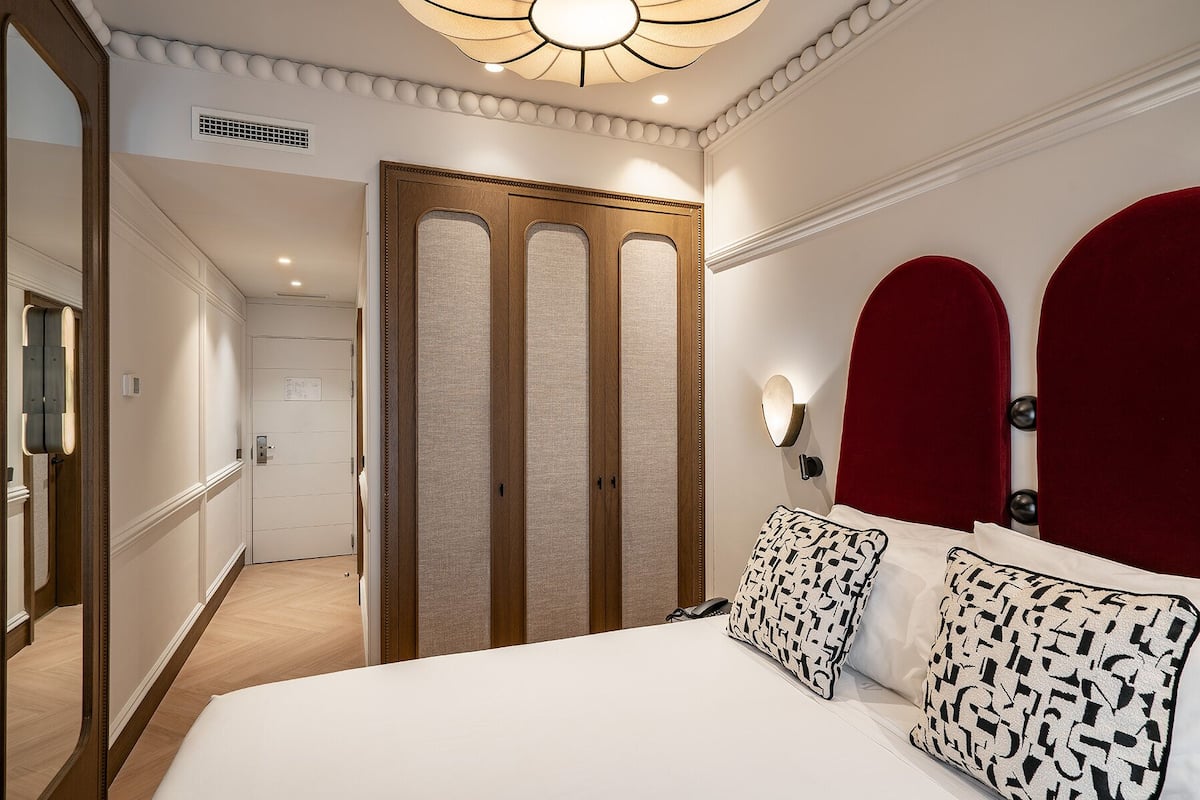 Une chambre d’hôtel avec un grand lit, une armoire en bois, un miroir et une tête de lit rouge.