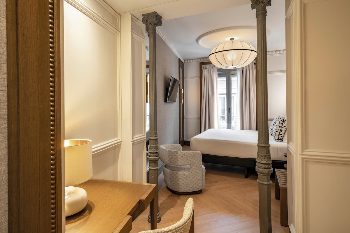 Une chambre d’hôtel avec un plancher en bois, un lit, une chaise, une table et un grand miroir.