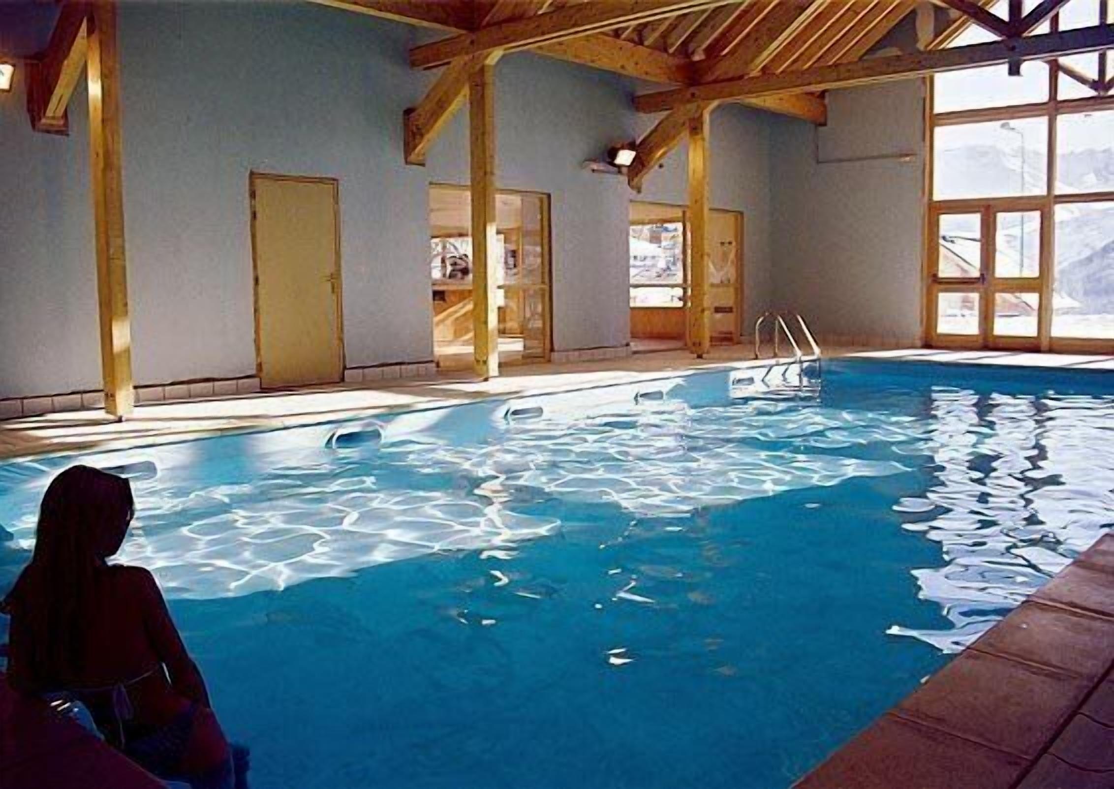 Ein Innenpool mit klarem, blauem Wasser, Holzbalken und großen Fenstern.