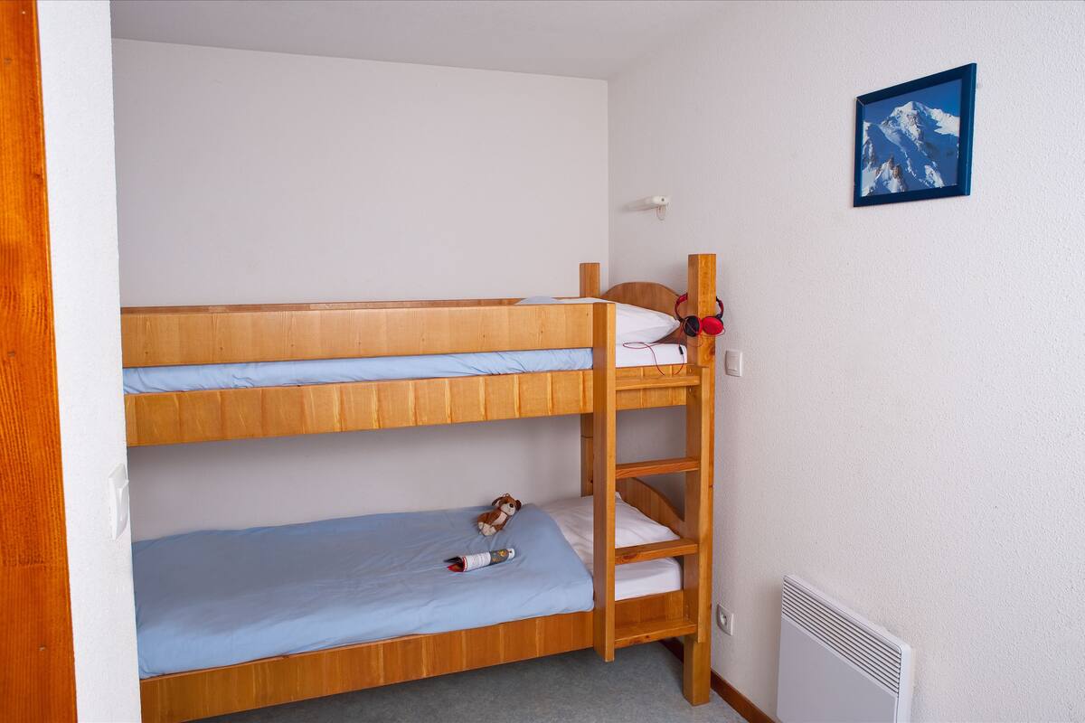 A bunk bed room with a wooden ladder, a small shelf, and a picture on the wall.