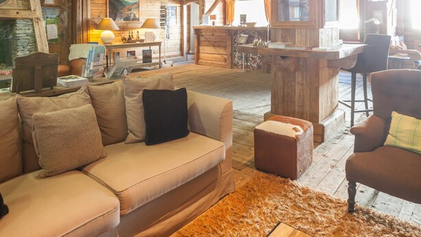 A rustic cabin interior with a wooden ceiling, a sofa, a coffee table with magazines, and a dining area with a table and chairs. - Residence Pierre & Vacances Premium L'Ecrin des Neiges (Tignes)