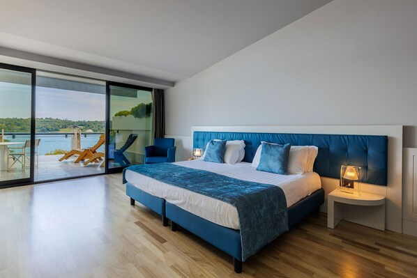 Une chambre moderne avec un grand lit, une table de chevet et une vue sur une étendue d’eau, visible à travers une porte vitrée.