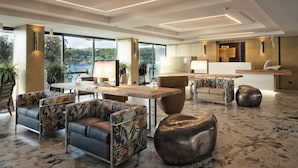 A modern hotel lobby with a marble floor, leather sofas, a wooden reception desk, and large windows offering a city view. - Hotel Salo' du Parc (Salò)