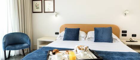 A hotel room with a bed, a chair, a tray with breakfast items, and two wall-mounted lights.