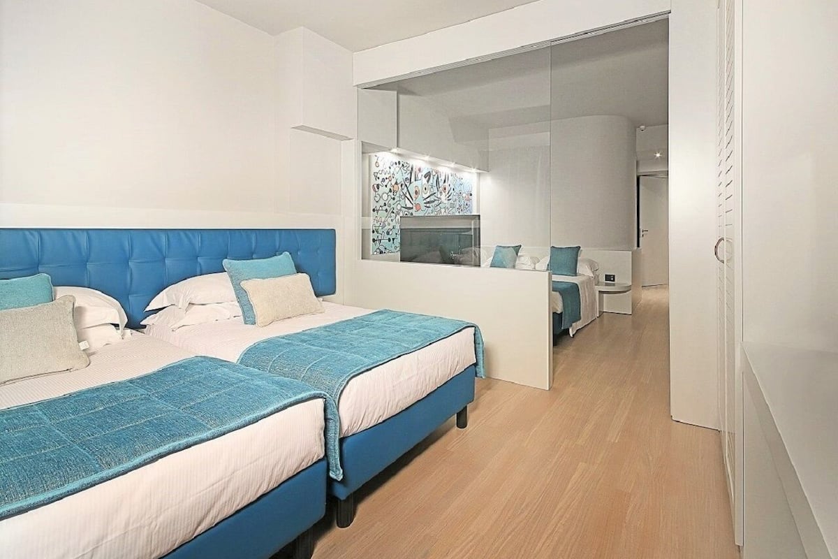A modern bedroom with two beds, a small desk, and a mirror.