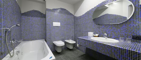 Ein Badezimmer mit Badewanne, Toilette und Waschbecken, mit blauen Mosaikfliesen an Wänden und Boden.