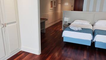 Quarto de hotel com duas camas, uma escrivaninha, uma cadeira, um criado-mudo com abajur e um guarda-roupa.