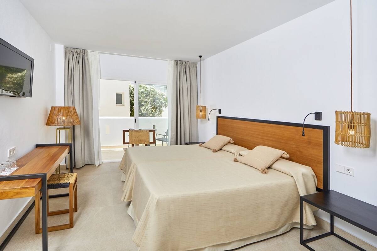 A modern hotel room with a large bed, a desk, and a chair. There is a television mounted on the wall and a window with curtains.