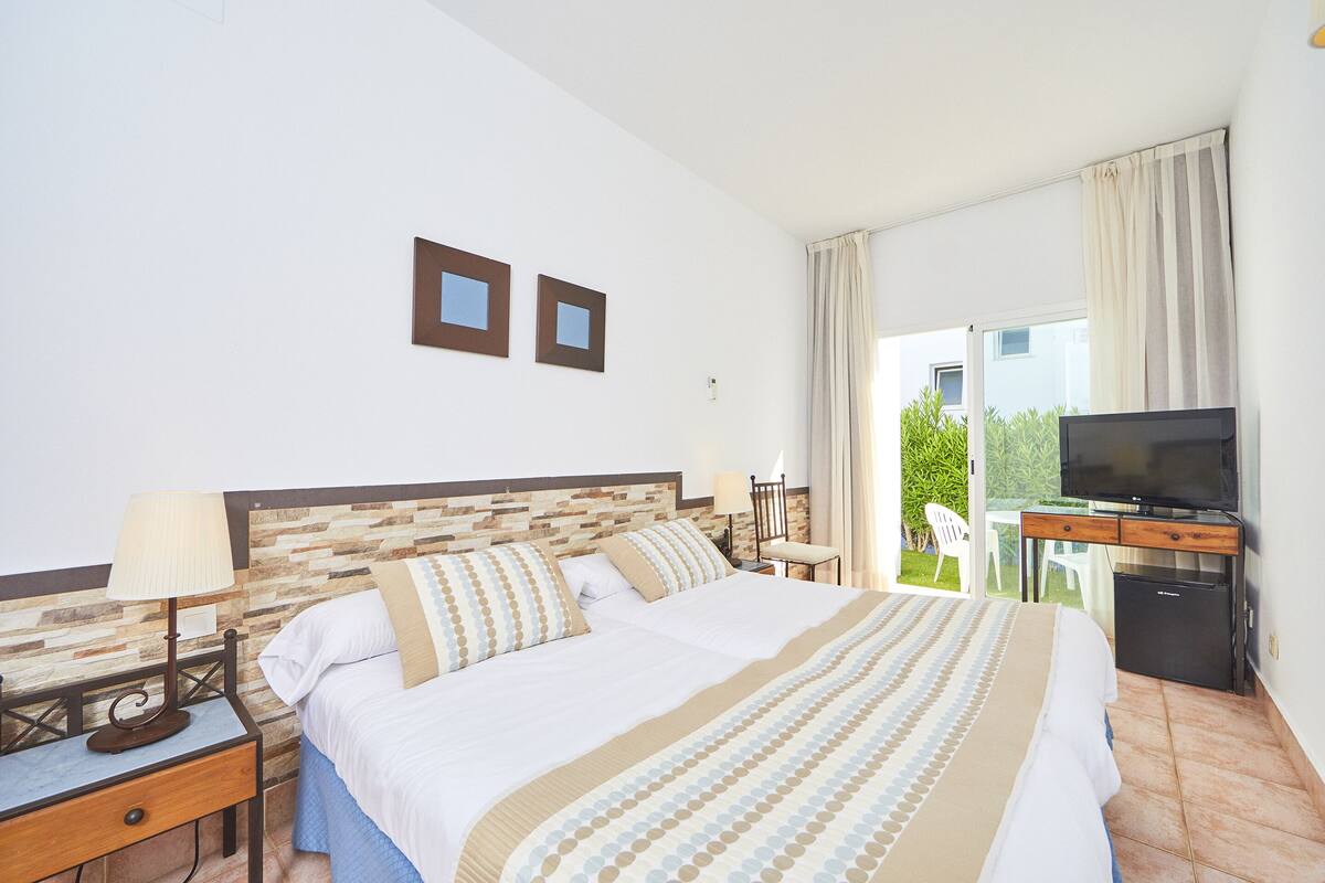 A hotel room with a large bed, a desk with a television, and a view of the outdoors.