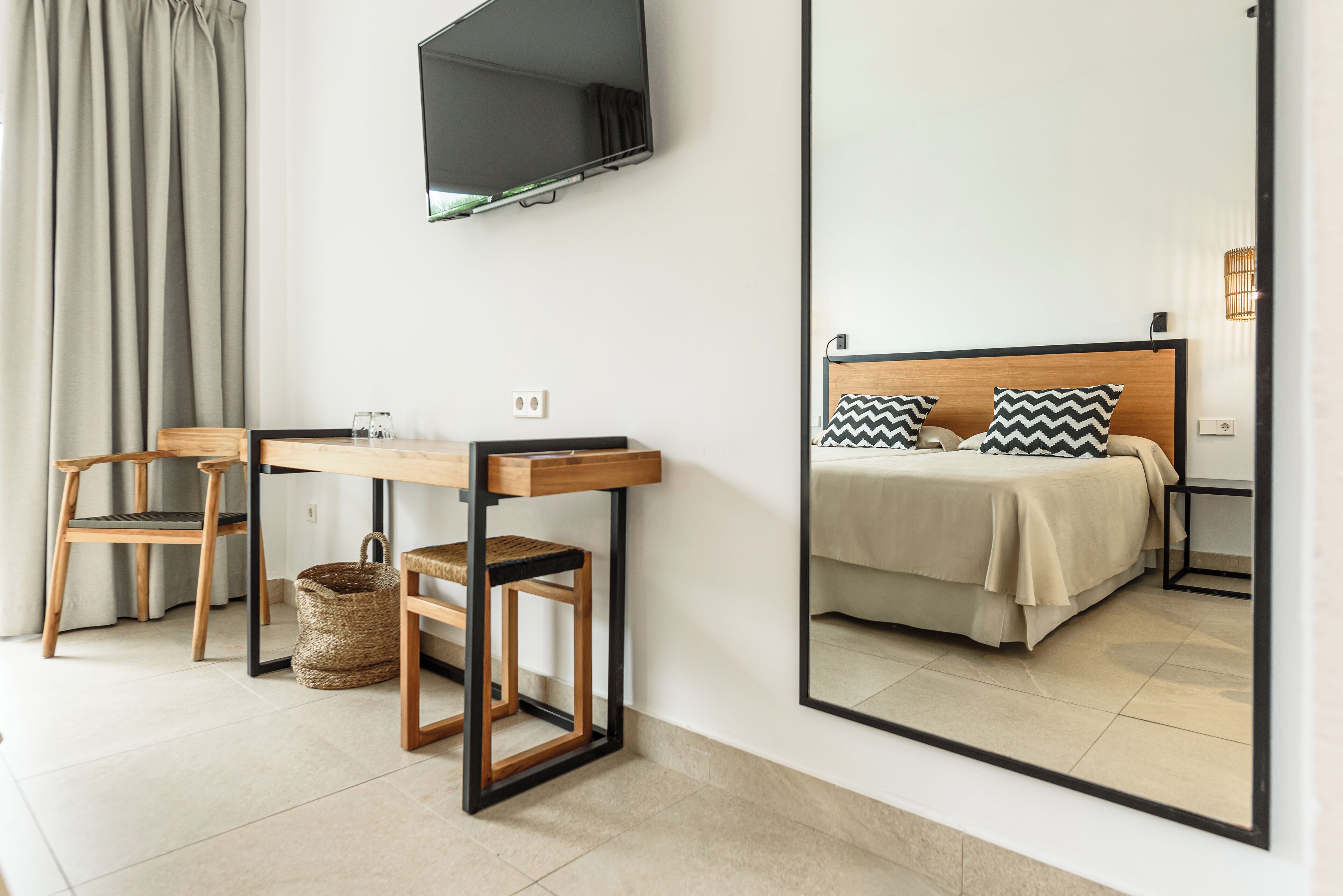 Una habitación de hotel con cama, escritorio, silla, televisión y un espejo grande.