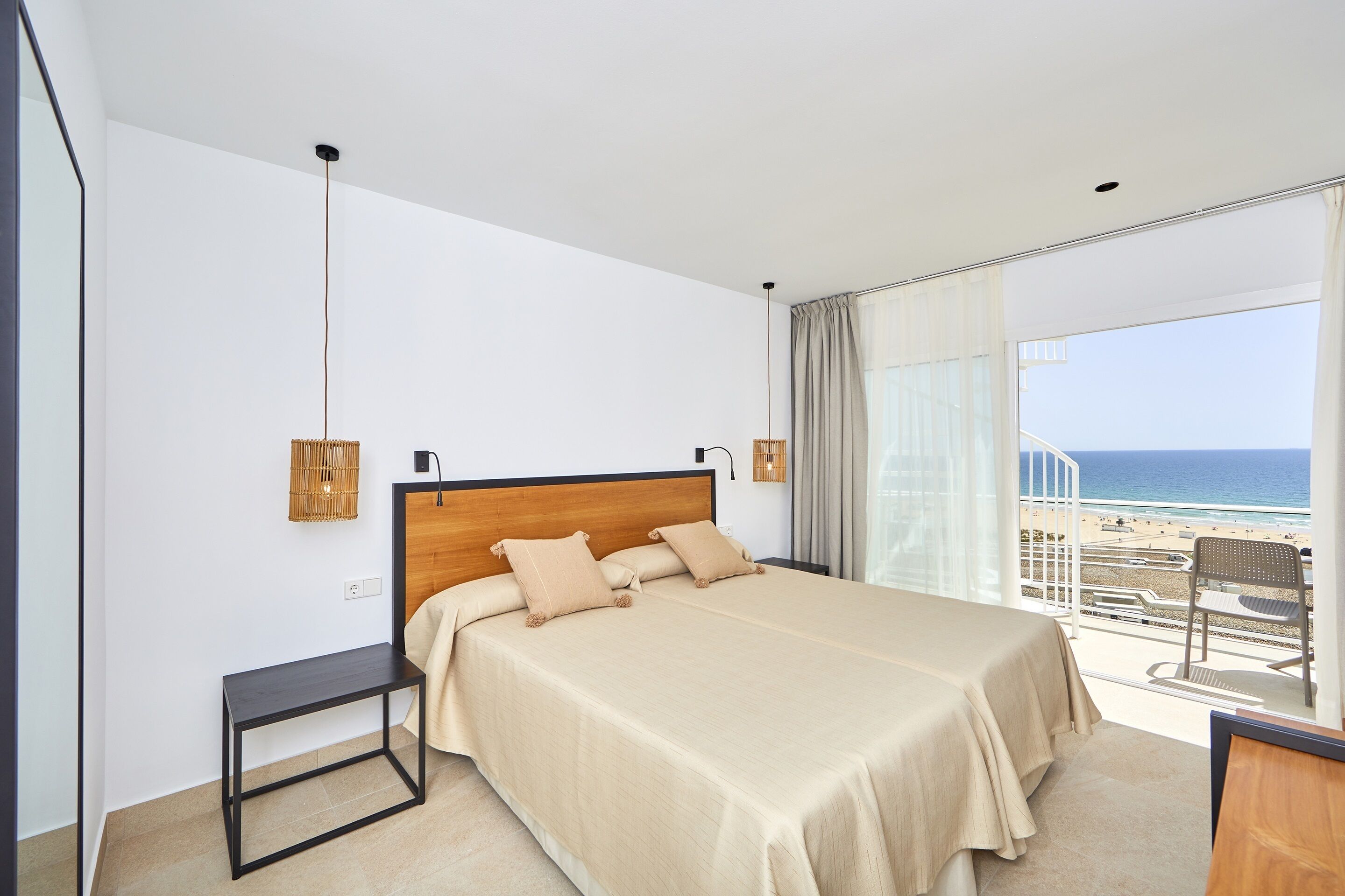 Ein Schlafzimmer mit einem großen Bett, einem kleinen Tisch und Blick auf den Strand.