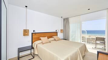 Ein Schlafzimmer mit einem großen Bett, einem kleinen Tisch und Blick auf den Strand.