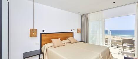 Un dormitorio con una cama grande, una mesita y vista a la playa.