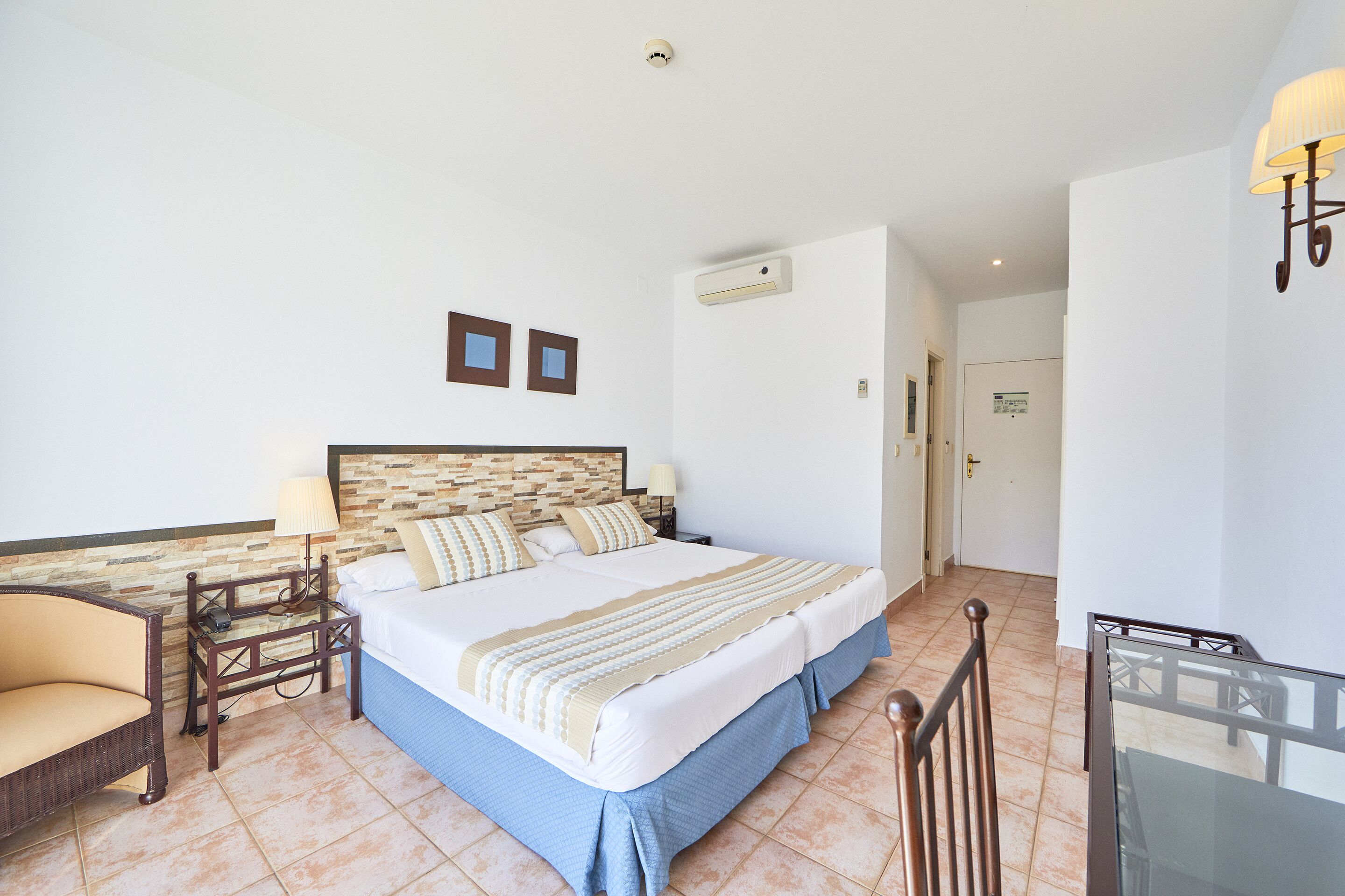 Una habitación de hotel con cama, escritorio, silla y mesa de vidrio.