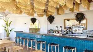 A bar area with a blue tiled wall, wooden stools, and hanging decorations. - FERGUS Conil Park (Conil de la Frontera)