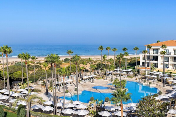 A resort with a large pool, palm trees, and a view of the beach.