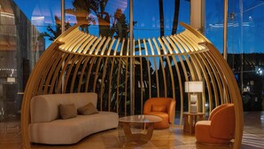 Un área de descanso moderna con una estructura de madera curva, un sofá, un sillón naranja y una pequeña mesa.