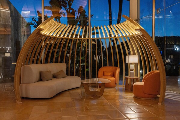 A modern lounge area with a curved wooden structure, a sofa, an orange armchair, and a small table. - Hipotels Barrosa Palace & SPA (Chiclana de la Frontera)