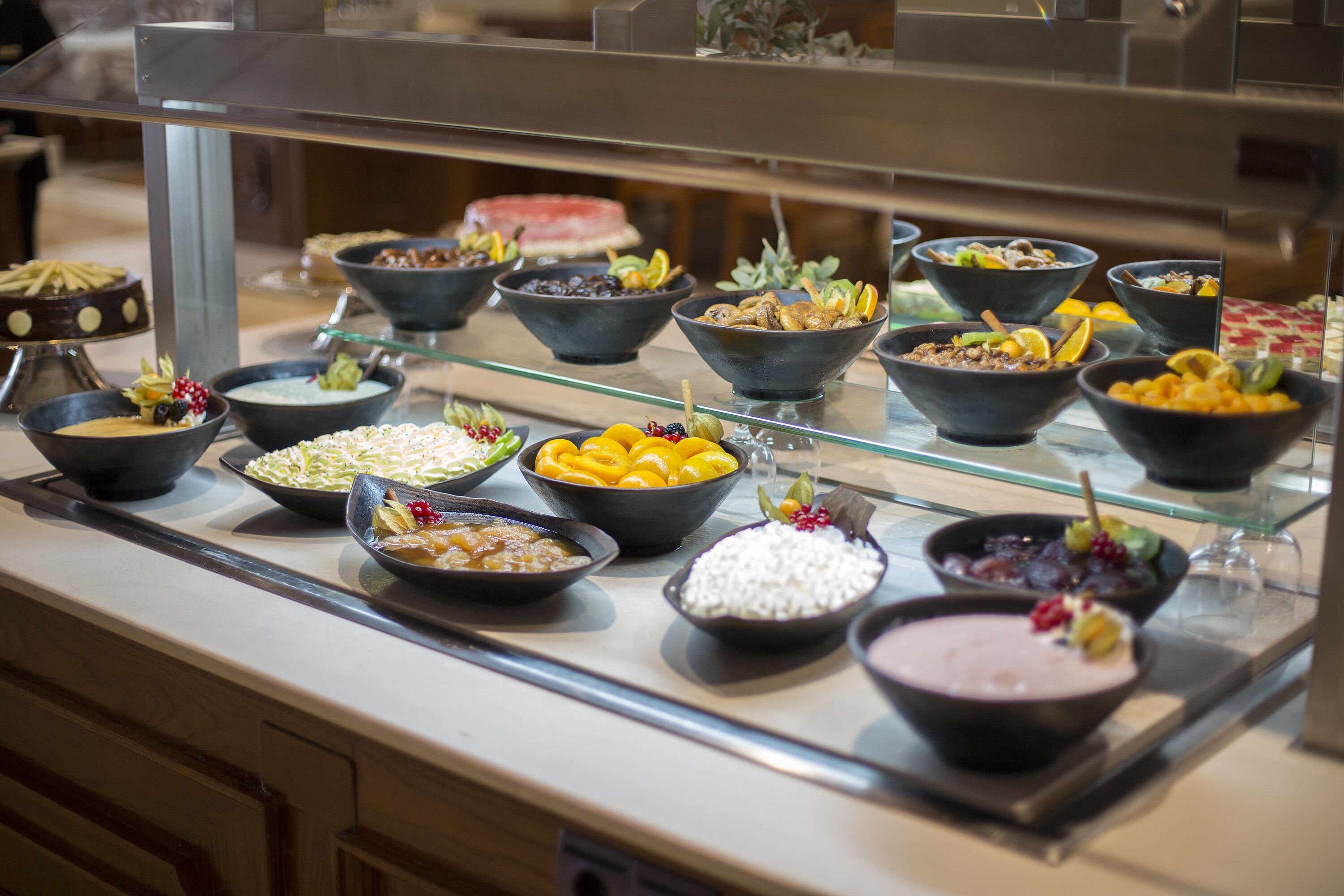A buffet with various dishes, including fruits, vegetables, and desserts, arranged on a glass display.