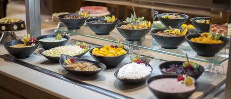 A buffet with various dishes, including fruits, vegetables, and desserts, arranged on a glass display.