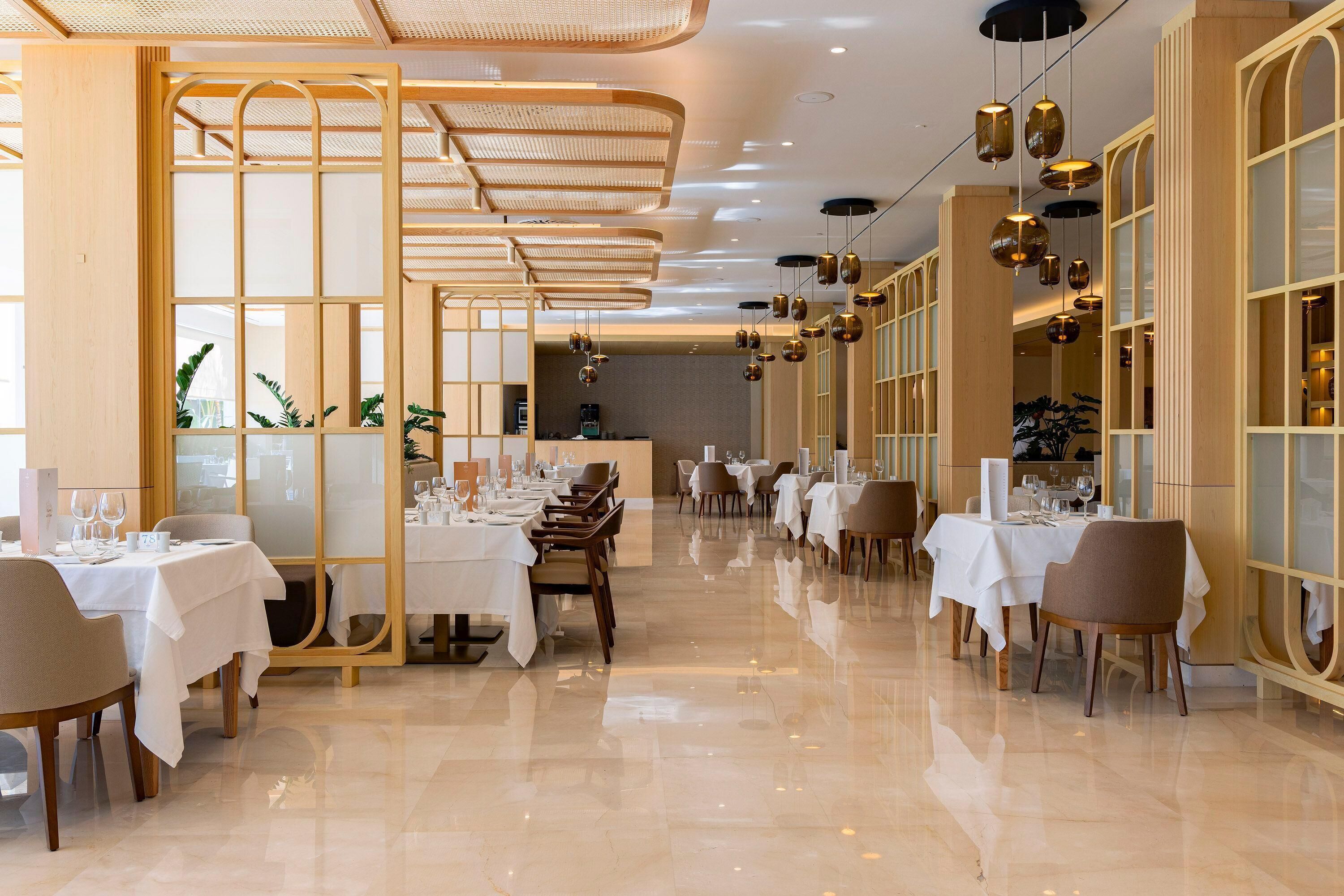 Un comedor amplio con varias mesas dispuestas para comer, con un diseño moderno y detalles de madera, y un suelo pulido.