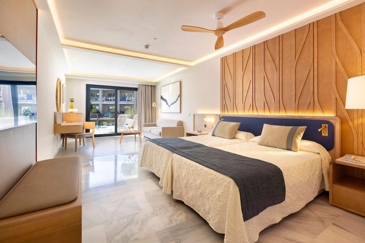 A modern hotel room with a large bed, a ceiling fan, a desk, and a view of the city.