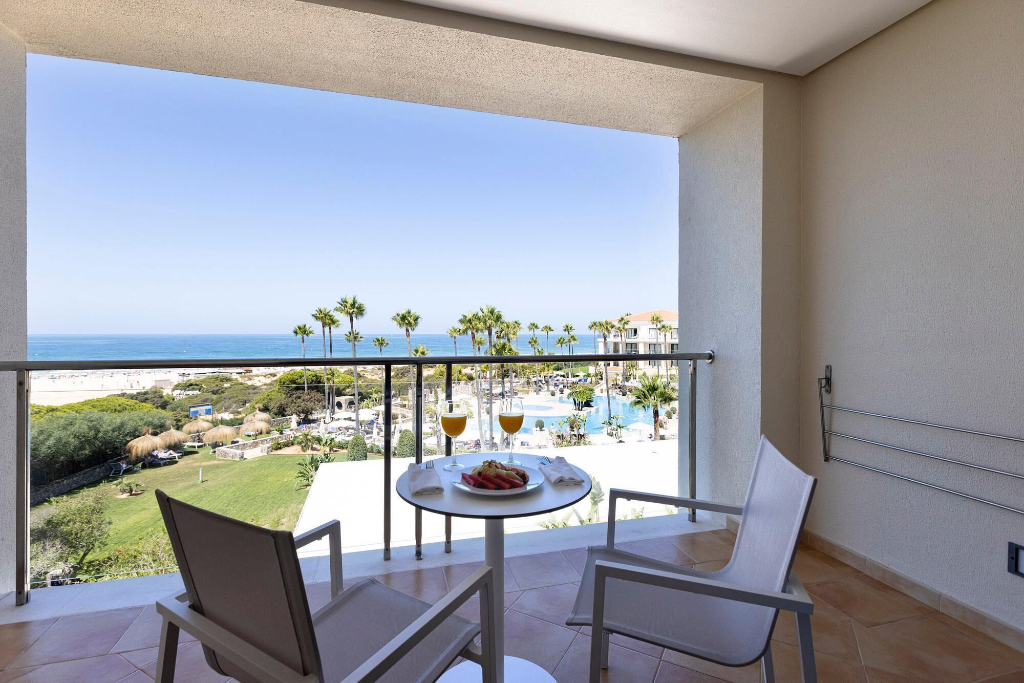 Un balcón con mesa lista para dos personas, con vistas a la playa y a la zona del resort.