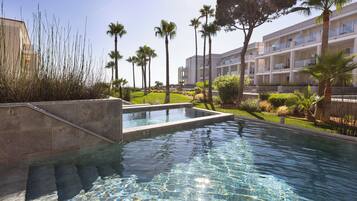 A swimming pool with clear water, surrounded by palm trees and a multi-story building with balconies.