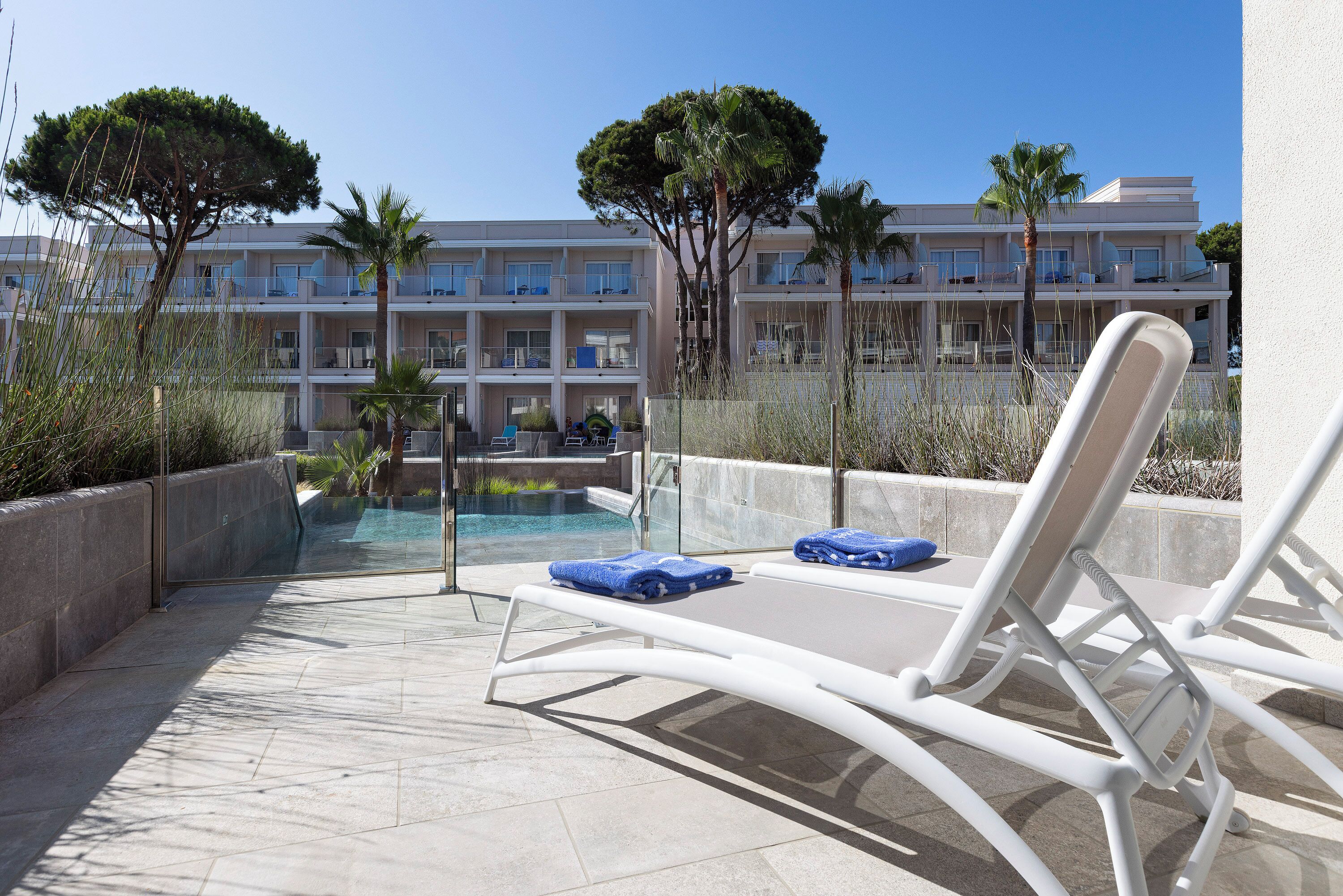 Ein Poolbereich mit Liegestühlen und freiem Blick auf ein Hotelgebäude im Hintergrund.
