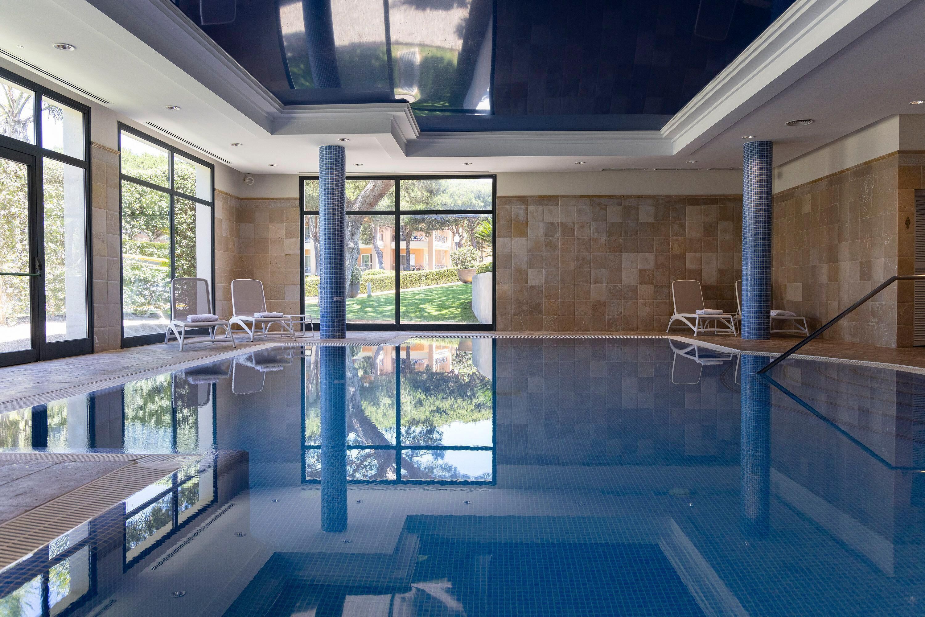 An indoor swimming pool with clear glass walls, a tiled floor, and a ceiling with skylights.