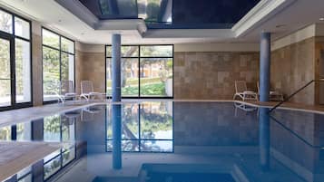 An indoor swimming pool with clear glass walls, a tiled floor, and a ceiling with skylights.