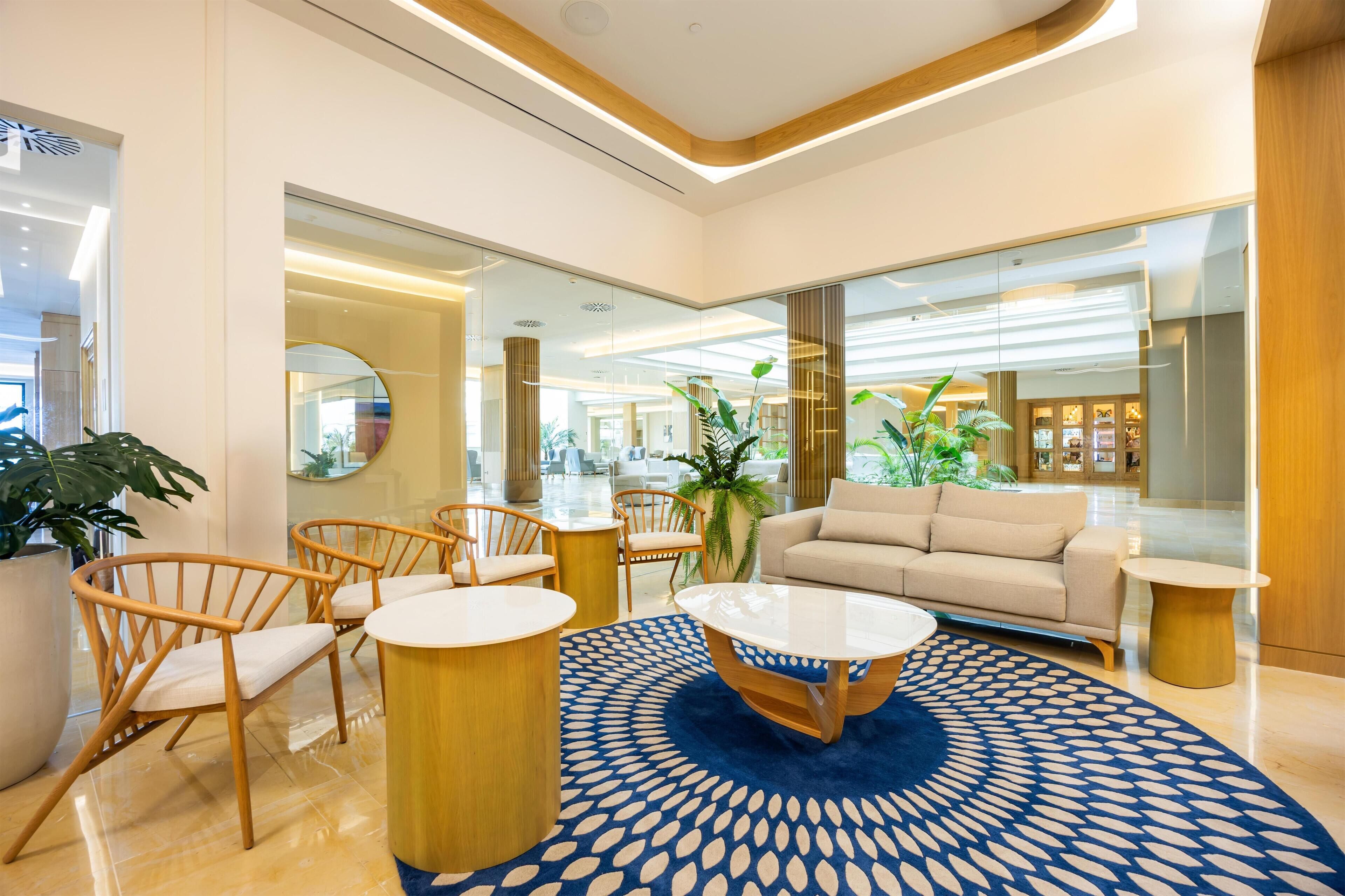 A modern lobby with a round coffee table, beige sofa, and wooden chairs.